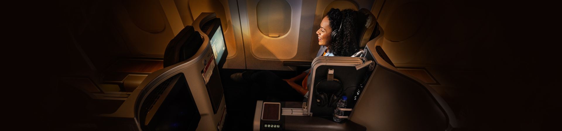 Smiling passenger, in Executive Class, sitting in a large, spacious and more comfortable chair, in a calm and dark environment, without people around it. You are watching some kind of entertainment on board, on the chair screen, with the TAP headphones put on.