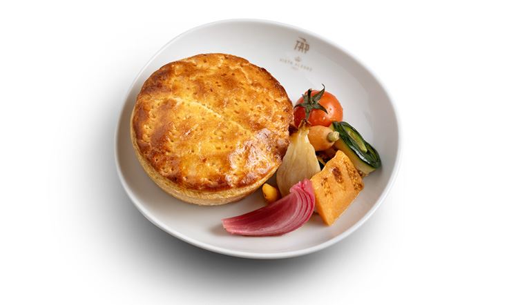 Photographie d'une assiette blanche, avec le logo doré TAP Air Portugal sur le bord, contenant une tarte au bar, flanquée à droite des légumes rôtis, à savoir des tomates, des carottes, des oignons, des courgettes, du potiron et du chou.